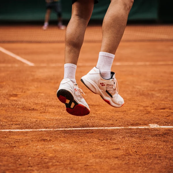 Low angle view of a tennis player jumping on a clay court, showcasing movement.